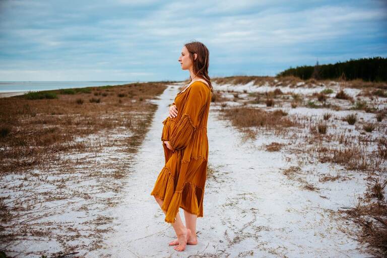 expecting mom holding belly on beach